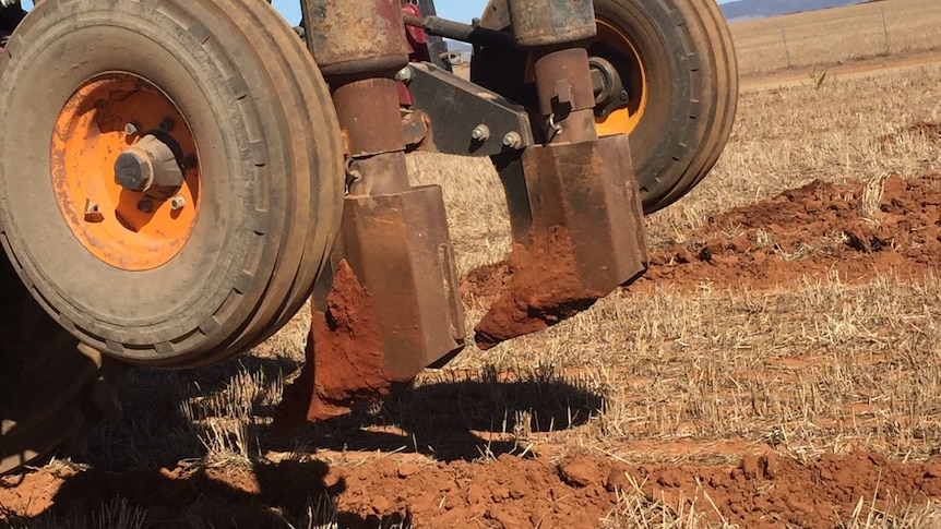 A piece of farm equipment on a red , dusty paddock.