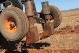 A piece of farm equipment on a red , dusty paddock.