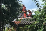 Two SES officers pull a tarp onto a roof.