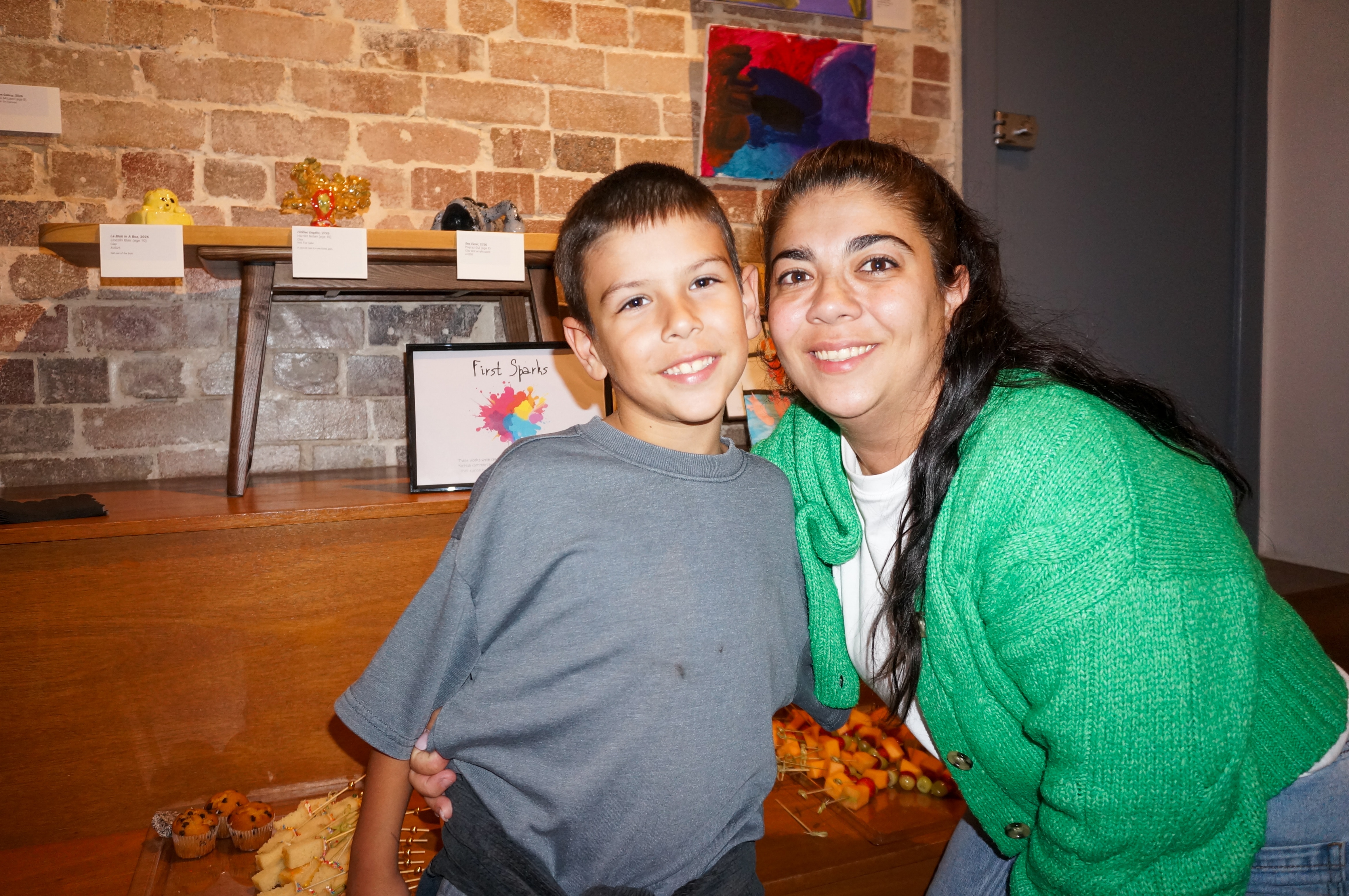 Мальчик улыбается женщине с длинным хвостом, одетой в зеленый кардиган.