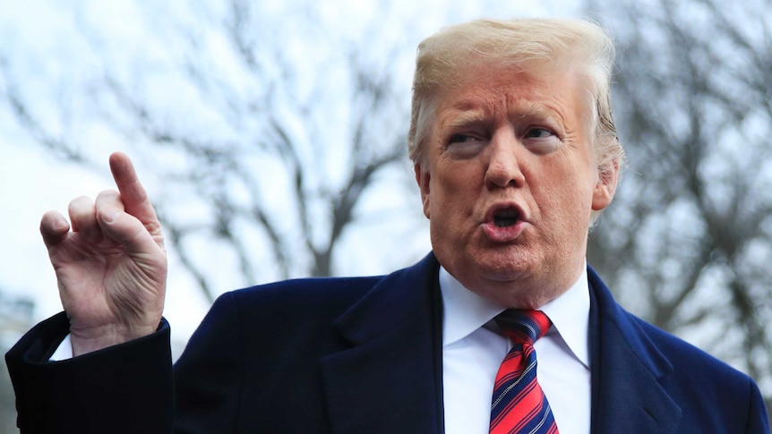 President Donald Trump points his right hand index finge as he addresses reporters at the White House in a navy suit.