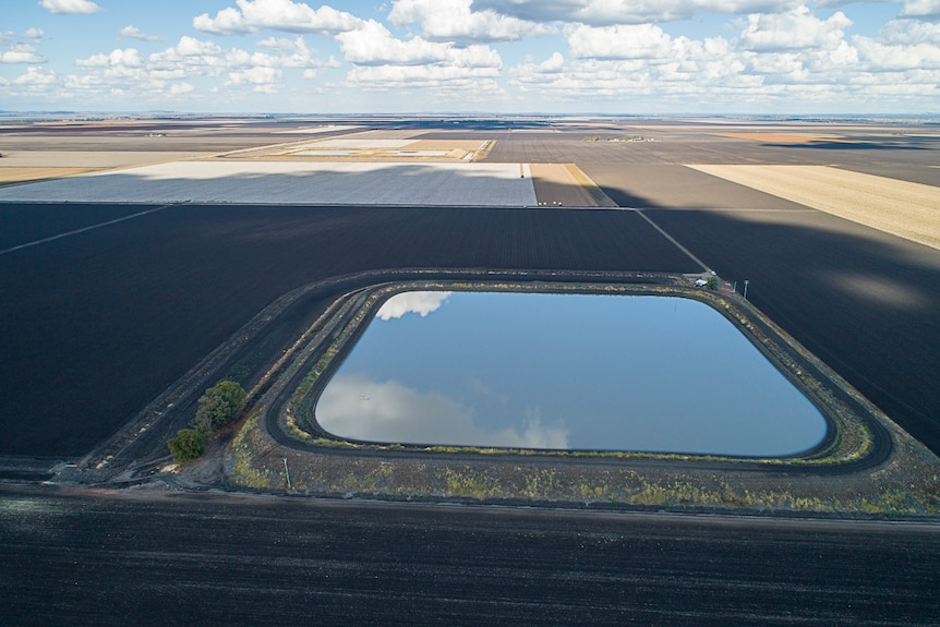 An aerial shot of an irrigation dam dam with a vast patchwork of paddocks behind.