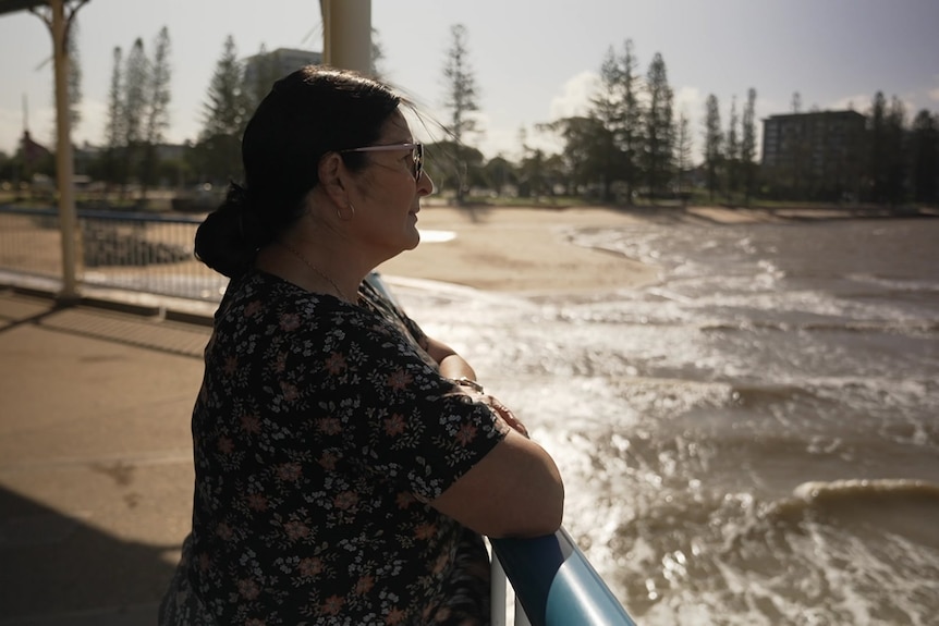 A woman with dark hair and glasses looks out off a pier.