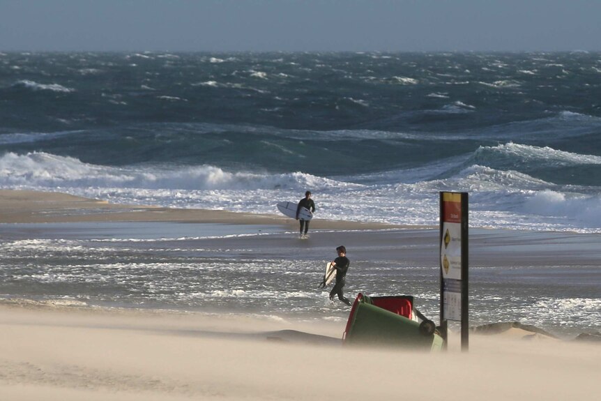 A storm has caused water to surge up over the beach at City Beach as two surfers leave the water