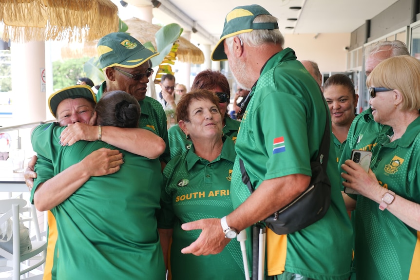 A crowd of people wearing green South African sports shirts stand in a group, smiling and hugging each other.