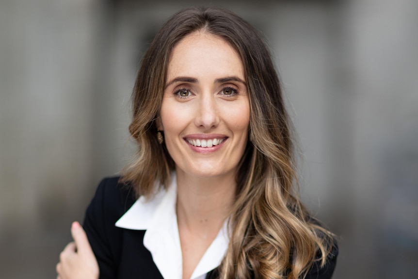 A smiling woman with long dark hair, wearing a dark blazer.