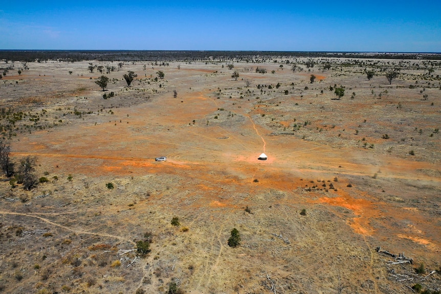An aerial photo of a car driving across a vast, dry and dusty paddock near Dirranbandi in south west Queensland, August 2023.