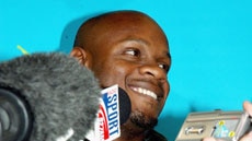 Asafa Powell is swamped by microphones after touching down in Melbourne