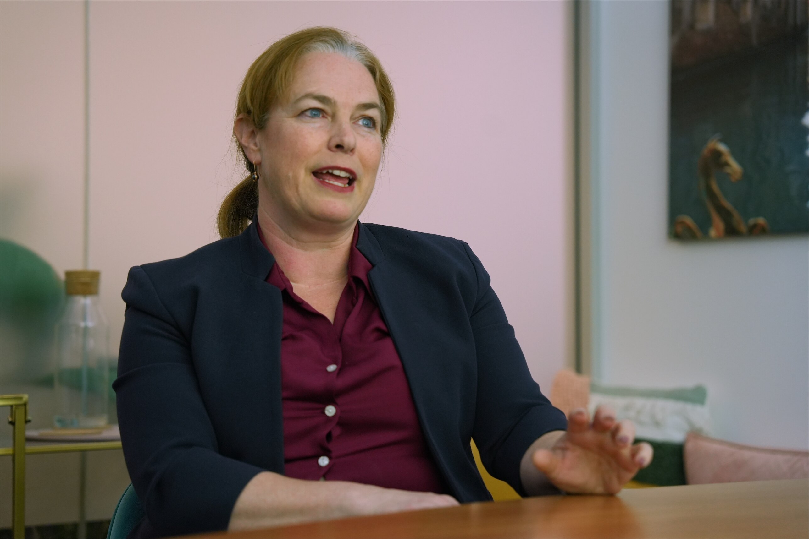 a woman with a blonde ponytail talking at her desk