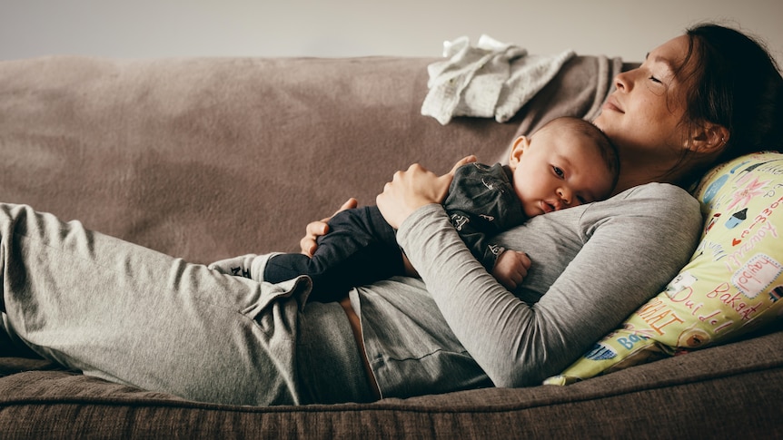 Mother sleeping on a couch with her baby on her