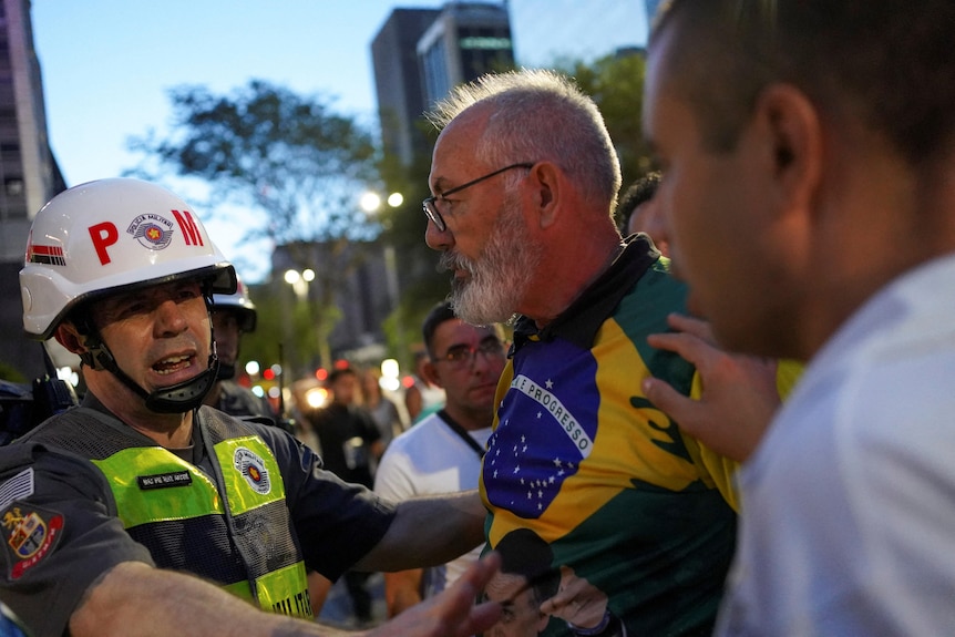 A protester wearing the colours of the Brazilian flag speaks with a police officer wearing a helmet