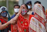 A woman in a red sari and a face mask is comforted by other women.