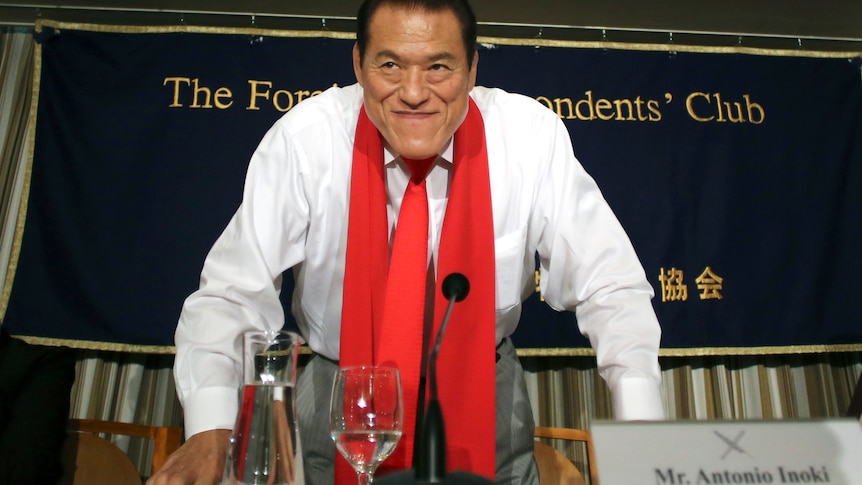 Antonio Inoki is standing with a red tie around his neck. 