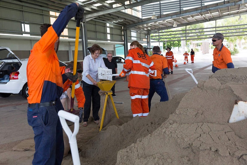 SES volunteers and council workers shovelling sand from a huge pile into bags.