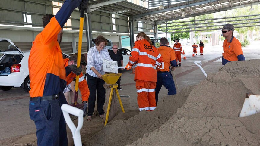 SES volunteers and council workers shovelling sand from a huge pile into bags.