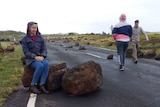 a woman sits on a large boulder which is lying across the road.