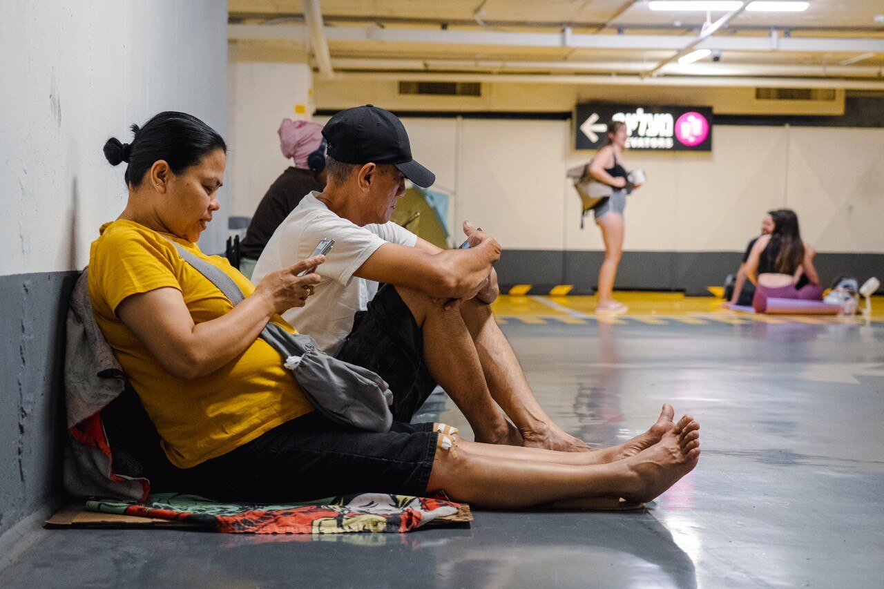 Two people siting on the ground of an underground car park, with one looking at their phone.
