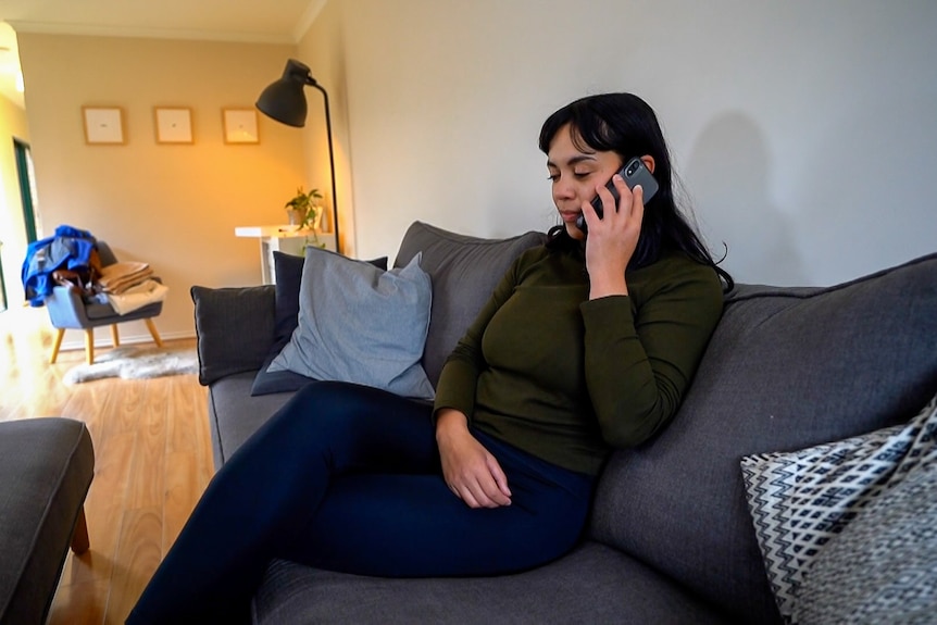 A young woman sits on a couch holding her mobile phone up to her ear.