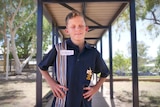 Young boy in school uniform stands with hands on hips smiling. Boy is vision impaired.