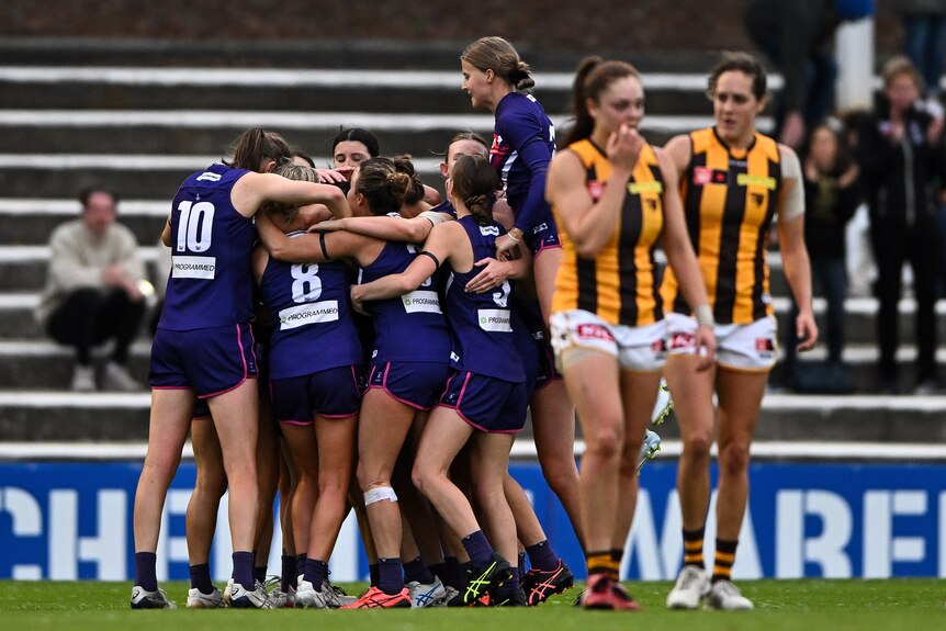 A group of Fremantle players celebrate in a huddle as Hawthorn players look disappointed
