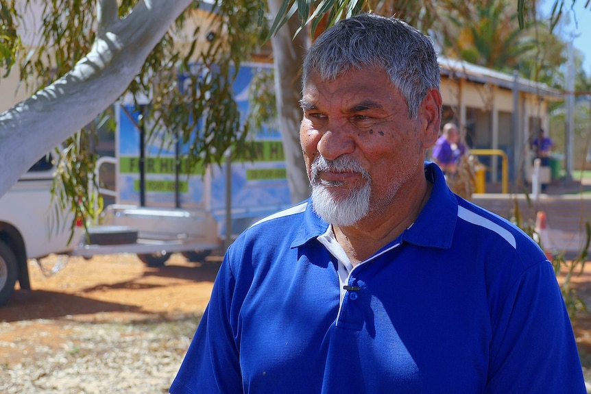 A man in blue stands under a tree