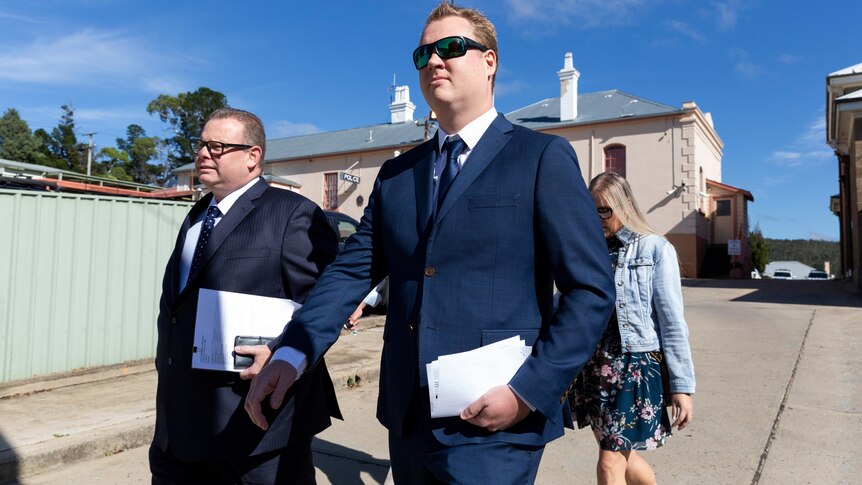 Two men wearing suits hold papers as they walk.