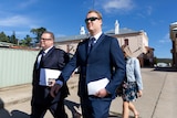Two men wearing suits hold papers as they walk.
