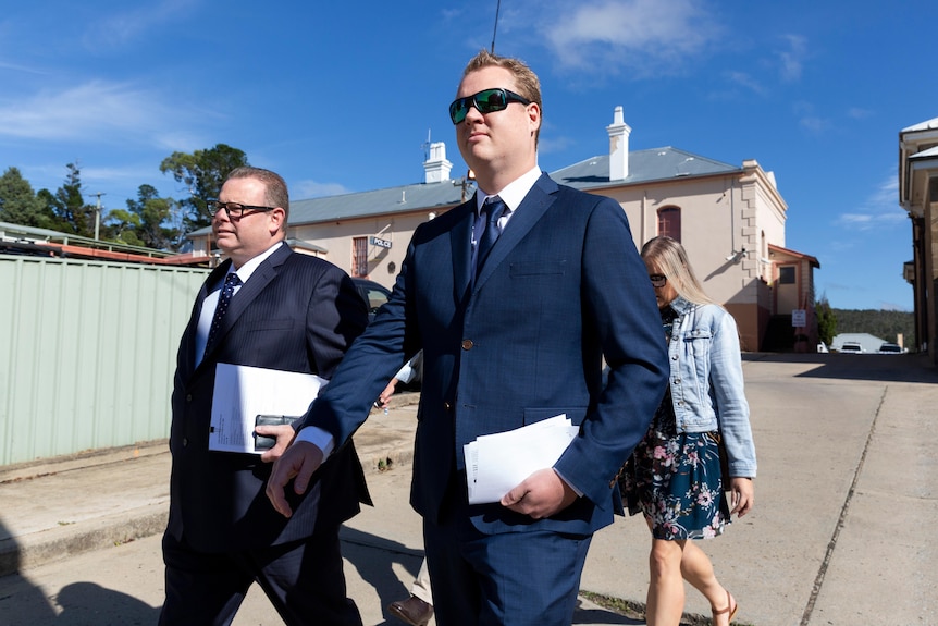 Two men wearing suits carry papers as they walk.