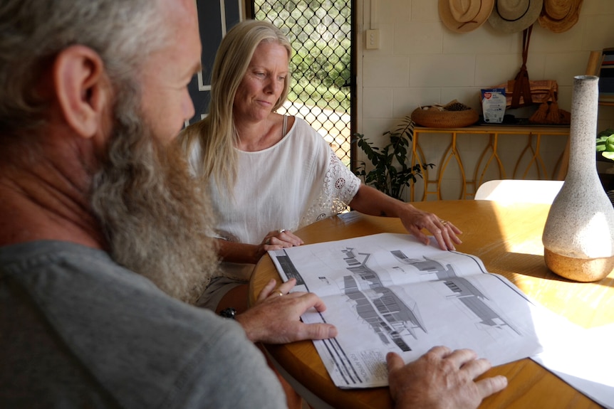 A man and woman sit at a table and look at design plans for a house