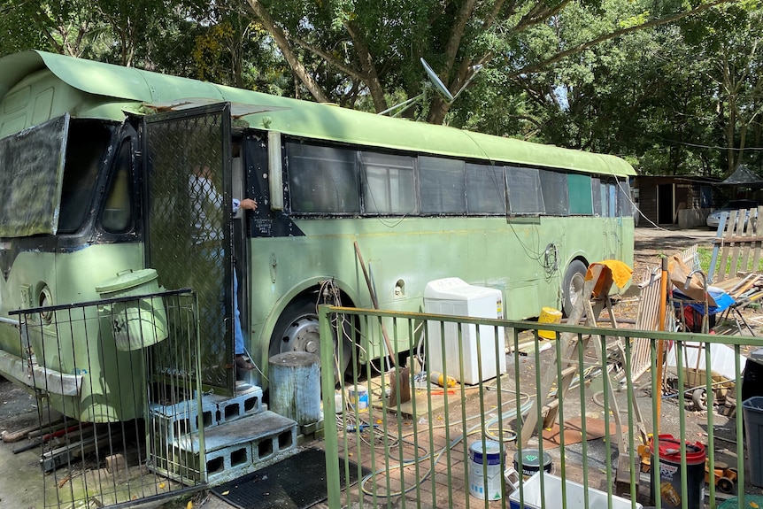 Green bus converted into a permanent home with a fenced yard, brick stairs and a washing machine outside.  