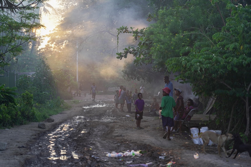 People walk down a muddy road lined with trees.