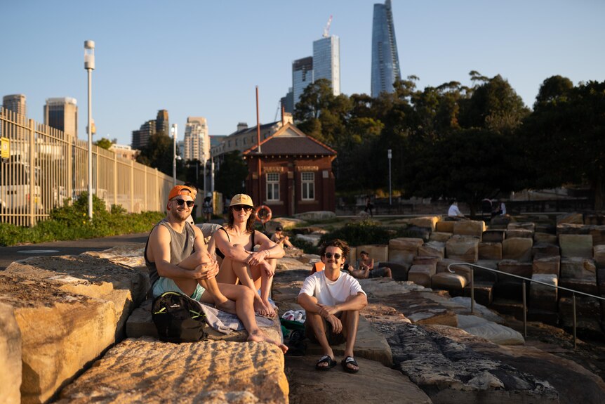 a group of three people sitting outdoors next to the water at sydney harbour