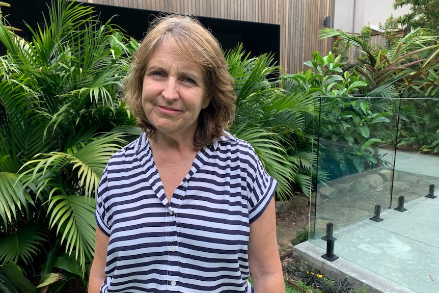 Woman in blue and white shirt with garden and home in background