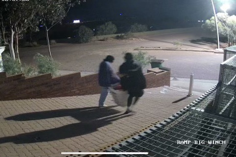 Two people holding a basket walking away from a business.