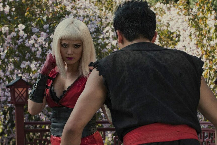 The two actors in street fighter style costumes face off in martial arts poses.
