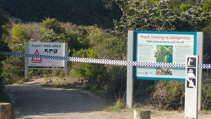 Police tape in front of a sign warning of the dangers of rock fishing.