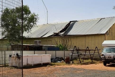 A large yellow warehouse with a part of its metal roof torn off after a storm.