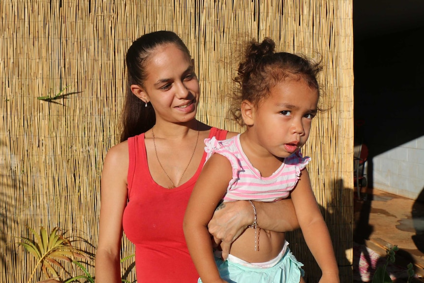 Caitlyn Roe carries her young daughter, who looks into the camera.