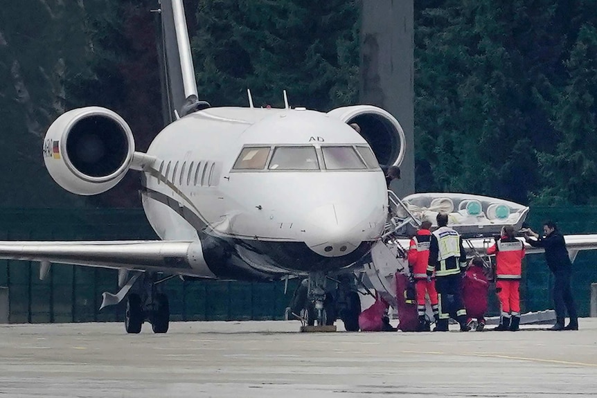 A medical team take a person on a stretcher from a parked aircraft.