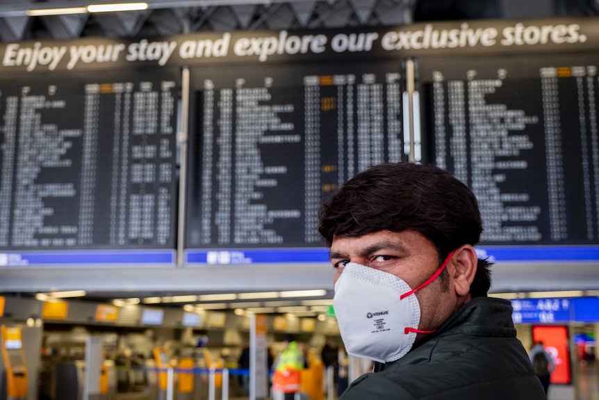 An Indian man in a face mask standing in front of a departures board at the airport