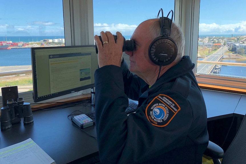 A man in a control tower looks through binoculars, with high views of Fremantle Port out the windows in the background.