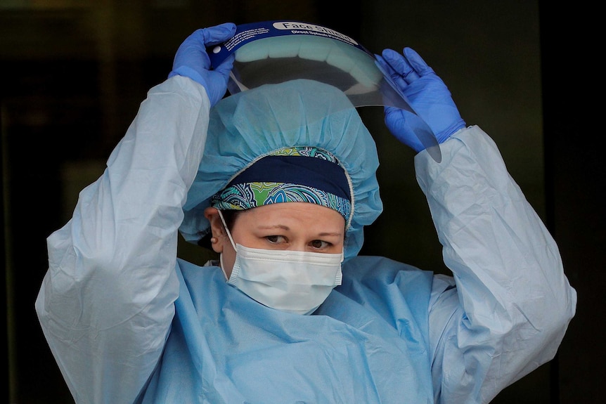 A close-up of a nurse lifting her face shield and looking worried