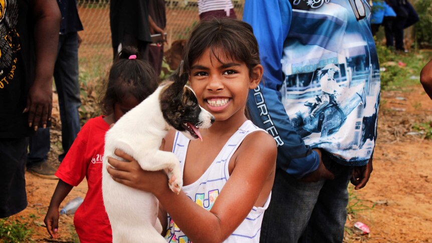 Indigenous girl holds up puppy smiling