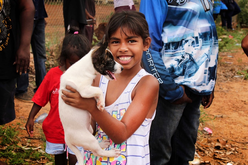 Indigenous girl holds up puppy smiling