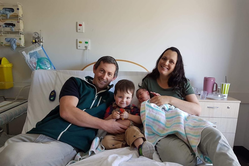 A family pose on a hospital bed with a newborn in a balnket