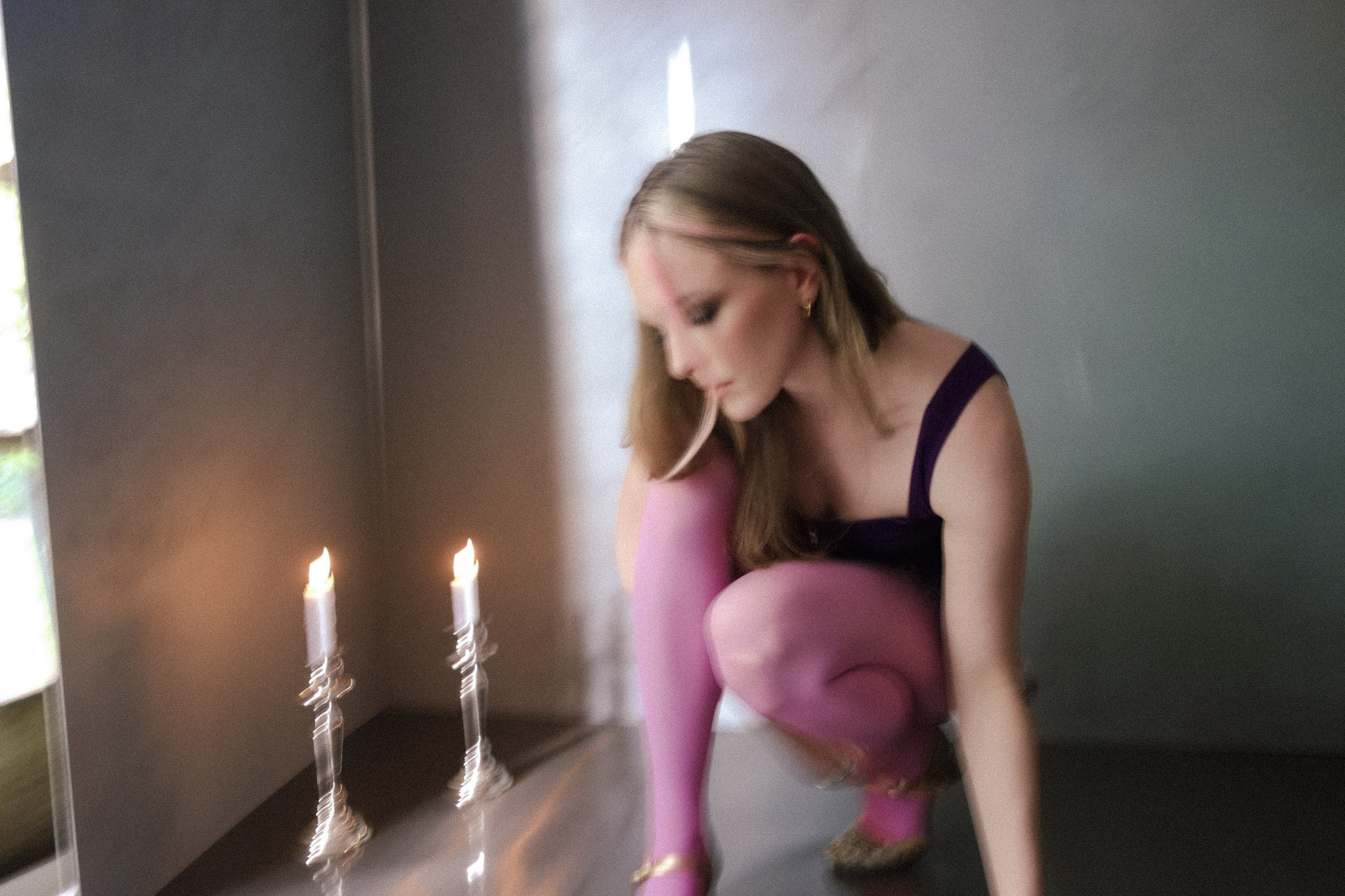 A blurry photo of a blonde woman in a black singlet and bright pink stockings next to two lit candles