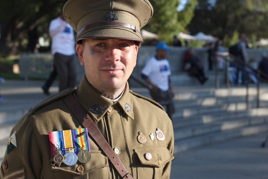 A mid shot of a man wearing war medals and a replica WWI uniform posing for a photo.