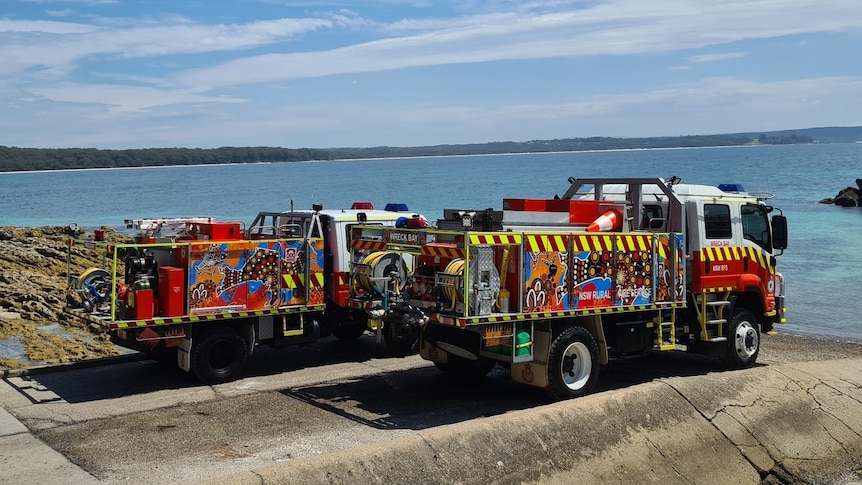 Two illustrated fire trucks stand are parked near a beach 