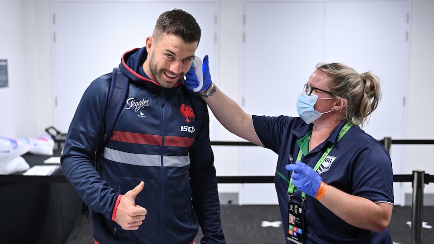 A woman puts a thermometer in the ear of Sydney Roosters fullback James Tedesco, giving a thumbs up, before an NRL game.