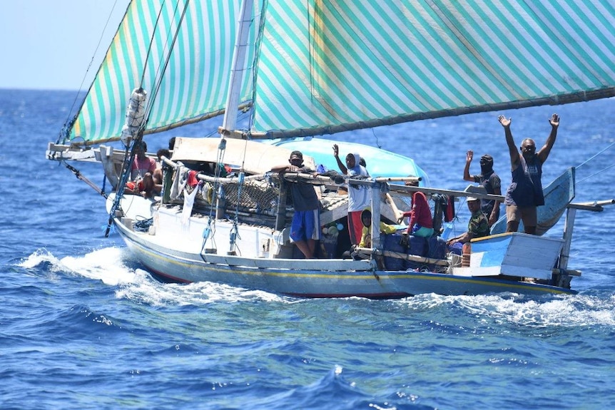 Indonesian fishermen wave at the camera from a fishing boat